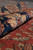 Rolled edge of the wool rug showing navy border palmettes and soft burgundy pile