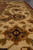 Angled macro of the beige border showing a gold rosette and dense wool pile