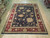 8'10" x 11'7" Chobi rug displayed flat on light hardwood, black field with red floral border