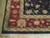 Corner detail showing burgundy main border, gold guard stripes, and cotton fringe on wood flooring