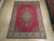8' x 11' Persian rug displayed on light wood showroom floor, red field, ivory border