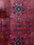 Bright red field with navy diamond medallion, orange rosettes and green leaf motifs woven in wool