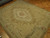 Angled floor view of the sage and cream needlepoint area rug with corner rose cartouches