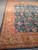 Angled corner view of the wool area rug where gold border meets teal floral field