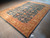 Brand new hand-knotted 9x12 rug lying flat with ivory fringe along the teal end