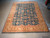 Hand-knotted Indian wool rug on warehouse floor, teal field framed by saffron gold border