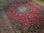Angled view showing deep red field, curling vine scrolls and dense wool pile of Tabriz rug