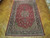 Red Isfahan rug photographed on parquet floor, full length view showing medallion and dark borders