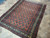 Vintage 1950s Persian village rug photographed at an angle on stone tile, coral and navy palette