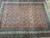 Angled view of indigo boteh motifs across the coral wool field and multi-band ivory borders