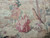 Close-up of two courtly figures in rose and pink robes woven into the landscape