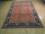 7'3" x 11' Sarough rug photographed at an angle, coral red field, ivory fringe, wood flooring