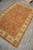 Diagonal view of hand-knotted Pakistani wool rug, cream border rosettes and coral floral field
