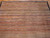 Angled view of striped wool rug showing salmon, rust, camel and slate blue stripe bands
