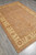 Full rug seen from the corner on grey floor, tan field framed by ivory border