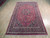 Hand-knotted wool Mashad rug photographed from the end, red field with dense floral vinework