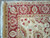 Corner close-up of coral red border with cream palmettes, camel guard stripe and hand-tied ivory fringe