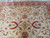 Sage green center lozenge and red rosettes across the ivory field of this square Indian rug