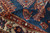 Rolled pile close-up revealing dense hand-knotted wool, indigo field and brick red geometric motifs