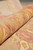 Rolled edge revealing dense hand-knotted wool pile in rust, gold and pink tones