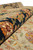 Rolled edge close-up revealing dense wool pile and border blossoms in gold, green, red