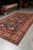 8x13 Kazak rug photographed at an angle showing red outer border and grey fringe