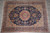 Overhead view of hand-knotted Kerman wool rug on grey tile, dense floral field and medallion