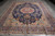 Full length 9x12 Persian Kerman rug photographed lengthwise showing beige spandrels, navy border and ivory fringe