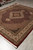 Room-ready 8 by 10 wool and silk area rug displayed on tile beside stacked inventory