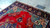 Daylight corner view on concrete, crimson field with teal floral spandrels and ivory fringe edge