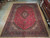 10 x 14 Persian Kashan rug displayed flat on wood showroom floor beside rolled rugs