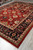 New 10x14 Mahal design rug angled on tile floor, rolled rugs stacked in the background