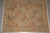 Soft beige garden rug displayed on grey tile floor showing dusty rose and faded blue lattice