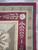 Corner detail of burgundy border with ivory rosette, laurel sprigs and checkered outer stripe band