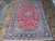 7'10" x 11'7" Persian rug displayed flat on stone tile floor, red field, navy borders