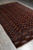 Full length diagonal view of the vintage burgundy Turkmen Yomut rug on grey flooring