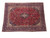 Large 10x13 Kashan rug displayed at an angle, red field inside deep navy floral borders