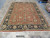 Overhead warehouse view of the hand-knotted 9x12 coral rug laid flat beside rolled inventory