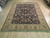 Hand-knotted wool rug shown at an angle, dark field framed by wide gold floral border