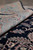 Rolled edge of the wool rug showing pile height and salmon border scrollwork detail