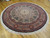 Angled floor view of 8x8 round hand-knotted rug with camel border and ivory fringe