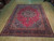8' x 11' Mashad rug displayed on light wood showroom floor, full medallion design visible