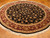 Round black Oriental rug on parquet floor showing maroon border, ivory guard bands and fringe