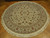 Angled view of cream round hand-knotted rug showing sage border, burgundy roses and cotton fringe