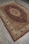Complete rug shown diagonally on grey floor, ruby field, ivory oval medallion, olive green corner spandrels