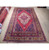 7x11 red Oriental area rug displayed on showroom floor with rolled inventory behind it