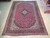Angled view of the 10x14 red Kashan rug showing navy border and floral corner brackets