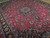 Angled view of raspberry red Tabriz field with dense vine scroll and dark palmette border