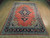 Angled floor view of the rug showing the open red field and the wide navy main border