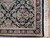 Corner detail showing burgundy border, ivory guard stripes and knotted cotton fringe against parquet